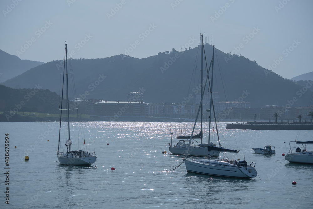 Naklejka premium sailboats anchored in a marina, with mountains in the background