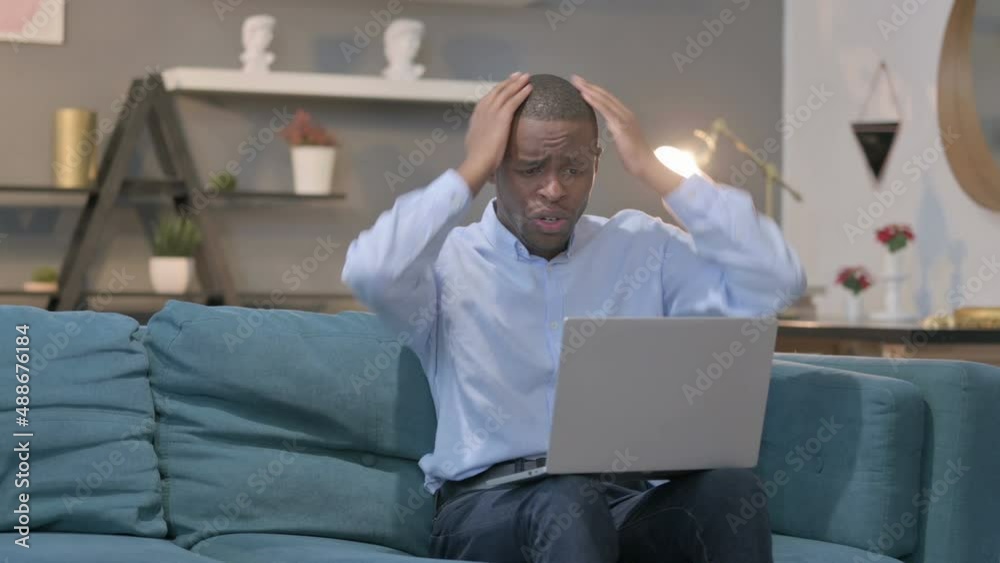 African Man with Laptop Reacting to Loss on Sofa African Man with Laptop Reacting to Loss on Sofa