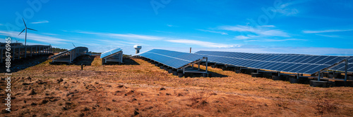 Clean energy installation or solar wind energy station. Photo-voltaic cell panels, a wind turbine, a water tank over the dried green field of wilderness. photo