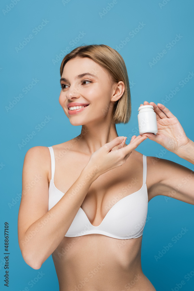happy young woman in white bra holding bottle with vitamins isolated on blue happy young woman in white bra holding bottle with vitamins isolated on blue