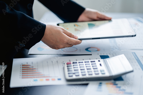 Close up of Businesswomen or Accountant using a calculator and laptop computer with analytic business report graph and finance chart at the workplace, financial and investment concept.
