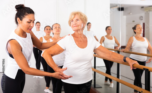 Various aged women exercising ballet dance moves. Woman trainer correcting her students.