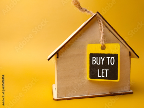 Foto Wooden house and wooden board with text BUY TO LET on a yellow background