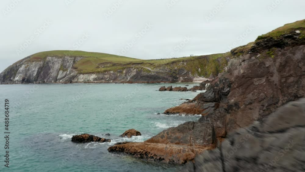 Fly over coastal rocks. Waves washing jagged sea coast. Revealing people on small sand beach under cliff. Amazing nature scenery. Ireland Fly over coastal rocks. Waves washing jagged sea coast. Revealing people on small sand beach under cliff. Amazing nature scenery. Ireland