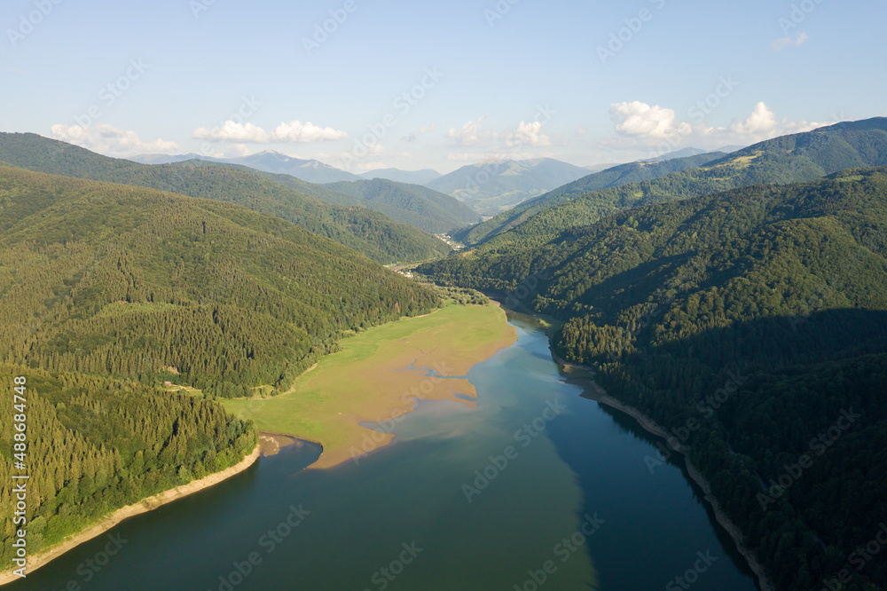 Aerial view of big lake with clear blue water between high mountain hills covered with dense evergreen forest