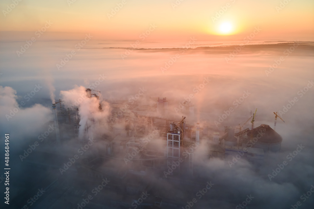Obraz premium Aerial view of cement factory with high concrete plant structure and tower crane at industrial production site on foggy morning. Manufacture and global industry concept