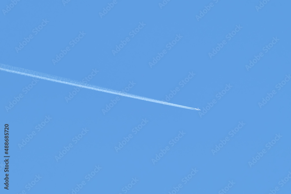 Distant passenger jet plane flying on high altitude on clear blue sky leaving white smoke trace of contrail behind. Air transportation concept Distant passenger jet plane flying on high altitude on clear blue sky leaving white smoke trace of contrail behind. Air transportation concept