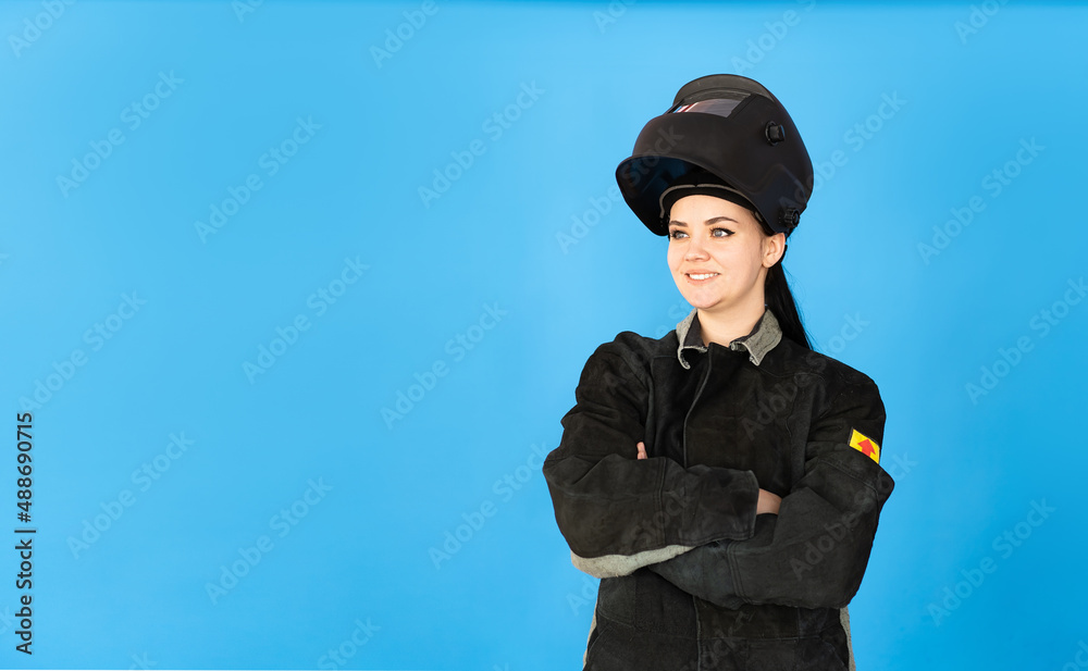 A female welder in a protective mask and a welder's suit on a blue background A female welder in a protective mask and a welder's suit on a blue background