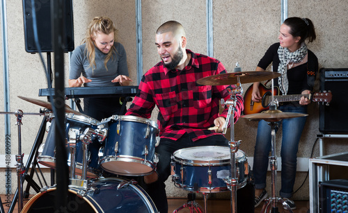 Group of young musicians with expressive male drummer rehearsing on rehearsal base photo