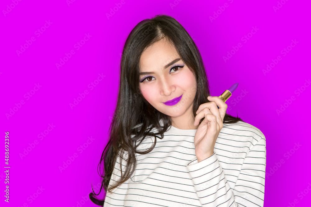 Beautiful Asian young brunette girl with curly hair applying pink lipstick on purple or ultraviolet background Beautiful Asian young brunette girl with curly hair applying pink lipstick on purple or ultraviolet background