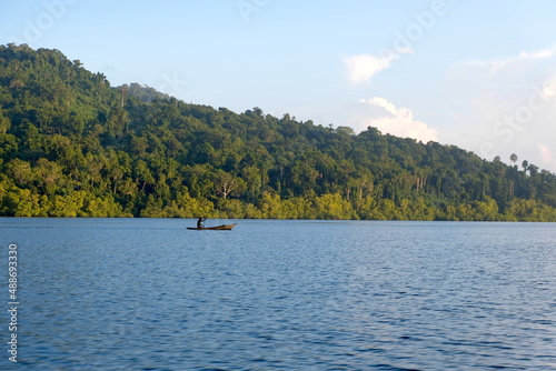 A person paddling a traditional fishing dugout canoe in the ocean with tree covered tropical island background in the Autonomous Region of Bougainville, Papua New Guinea