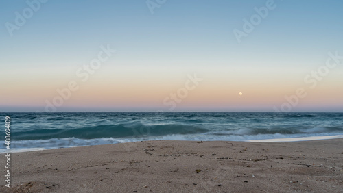 Evening on the Red Sea beach. Turquoise waves roll on the sandy shore. The moon is shining in the pink-blue sky. There is no one. Silence. Egypt