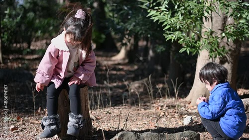 A boy picking up nuts and playing and a girl laughing on a log