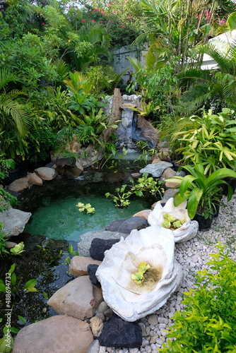 Beautiful landscaped tropical island garden hideaway with densely populated plants, waterfall, pond and flowers