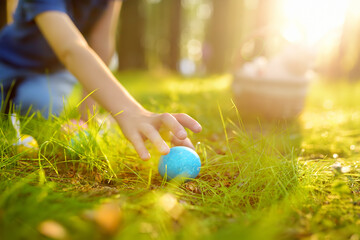Little boy hunting for egg in spring garden on Easter day. Traditional easter festival outdoors. Focus on multicolor eggs.
