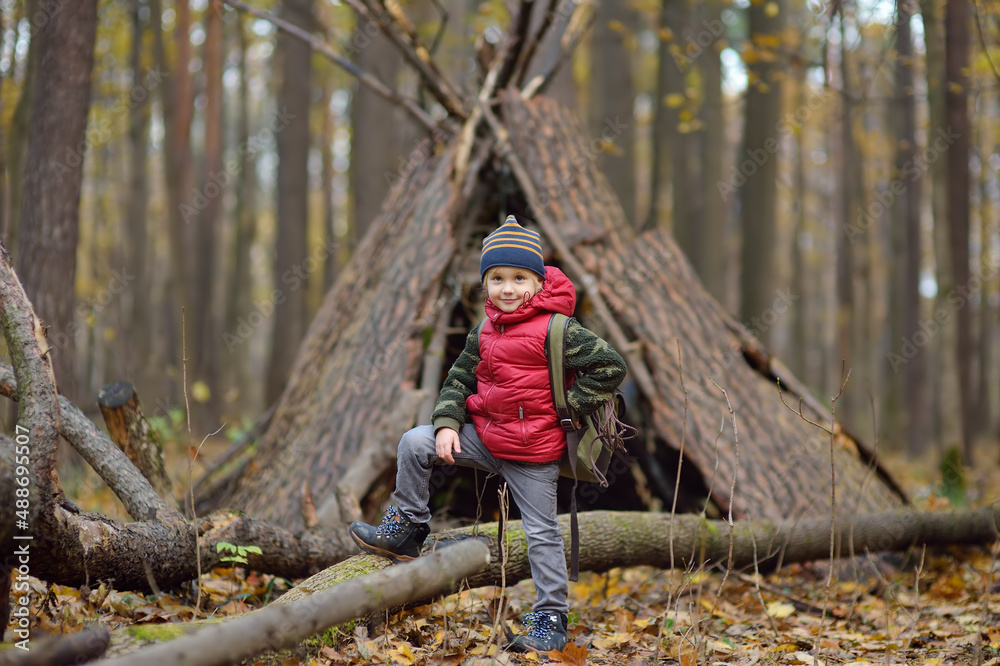 Little boy scout during hiking in autumn forest. Behind the child is teepee hut. Adventure, scouting and hiking tourism for kids. Little boy scout during hiking in autumn forest. Behind the child is teepee hut. Adventure, scouting and hiking tourism for kids.