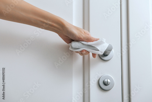 Cleaning door handles with an antiseptic wet wipe and gloves. Sanitize surfaces prevention in hospital and public spaces against corona virus. Woman hand using towel for cleaning home room door link