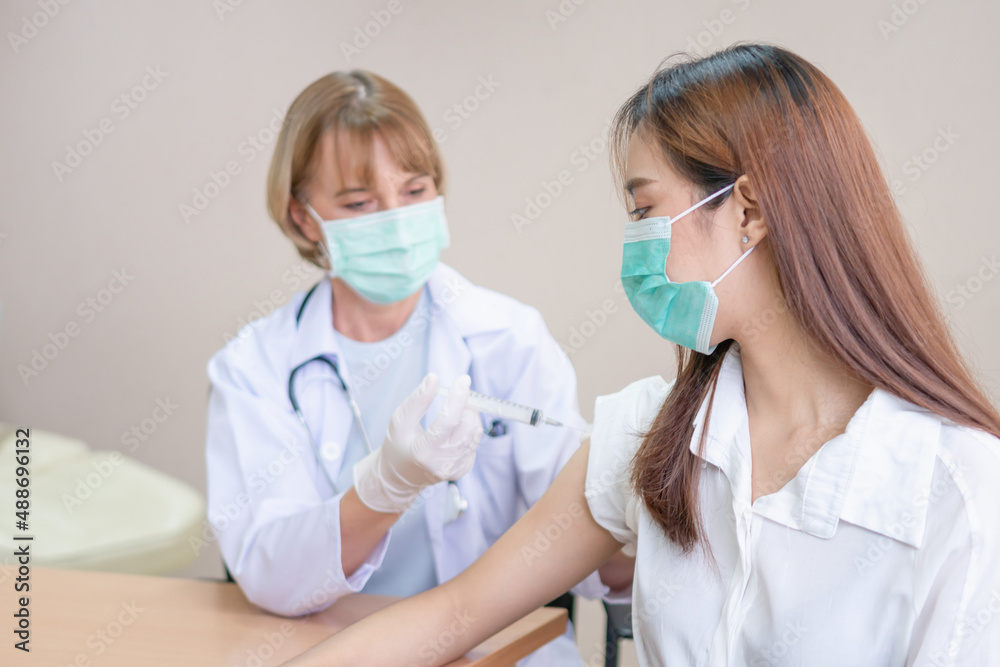 Doctor vaccinating young female patient in hospital, Woman in medical face mask getting antiviral vaccine at hospital Doctor vaccinating young female patient in hospital, Woman in medical face mask getting antiviral vaccine at hospital