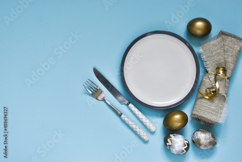 Easter table setting with decorative eggs, plate, napkin and cutlery on blue table. Elegance dinner. Top view. Space for text. Holidays background. Easter table.