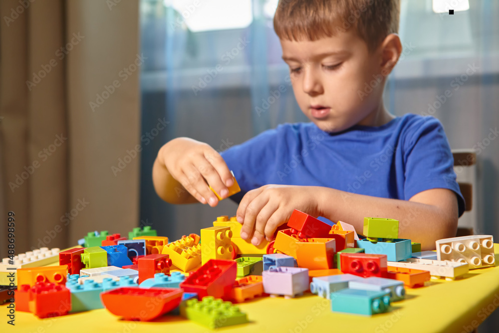 A beautiful boy is playing at home with building blocks. A cute smiling boy is playing with a constructor with a lot of colorful plastic blocks in the room, building a city. Preschool classes. A beautiful boy is playing at home with building blocks. A cute smiling boy is playing with a constructor with a lot of colorful plastic blocks in the room, building a city. Preschool classes.