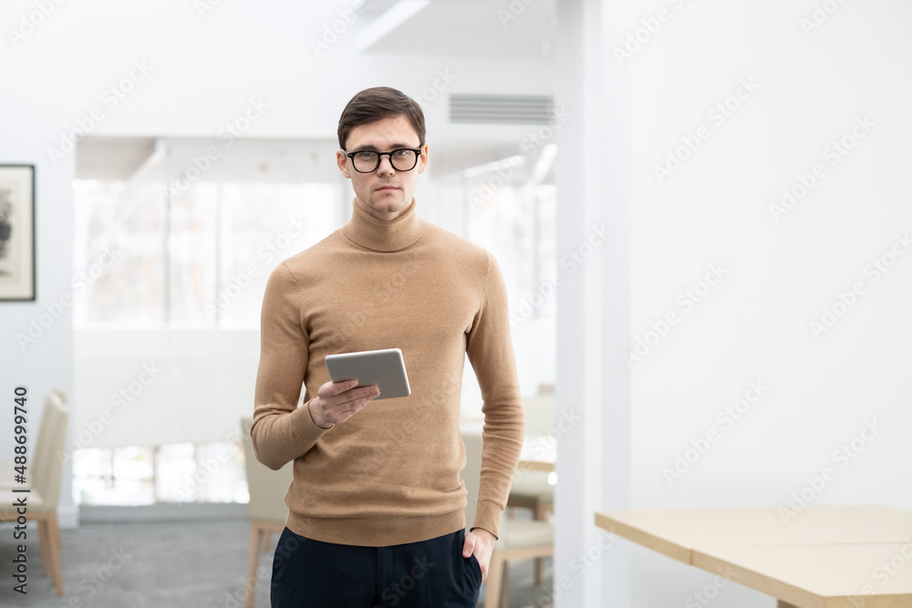 Obraz premium Young confident entrepreneur in smart casualwear holding digital tablet while working in the internet and analyzing online data