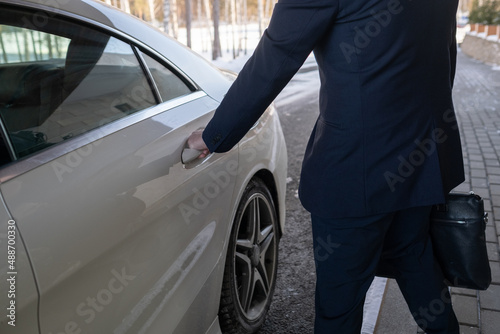 Contemporary elegant businessman in suit holding by handle of vehicle door while going to open it and get into car to drive to work © pressmaster