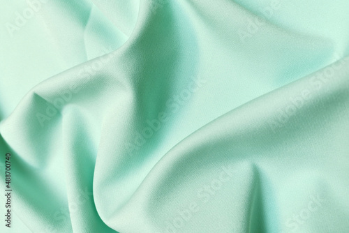 Green crumpled or wavy fabric texture background. Abstract linen cloth soft waves. Silk atlas or stretch jacquard. Smooth elegant luxury cloth texture. Concept for banner or advertisement.