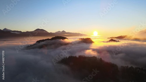 Normal drone footage in Bled Slovenia captured at sunrise with in the nature with beautiful mountains and landscapes cover in fog and nice golden hour colors filmed in  dynamic movement from above photo