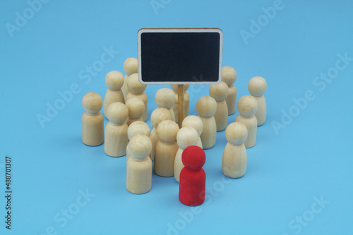 People meeting or protest concept. Wooden people figures with leader and chalkboard on blue background.