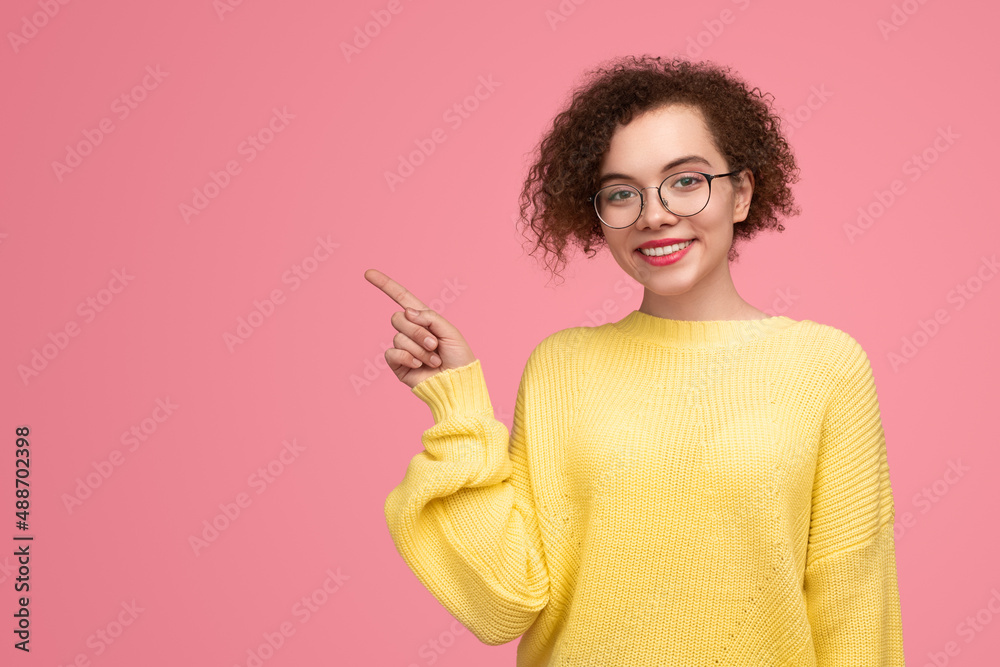 Content young lady pointing away in pink studio Content young lady pointing away in pink studio