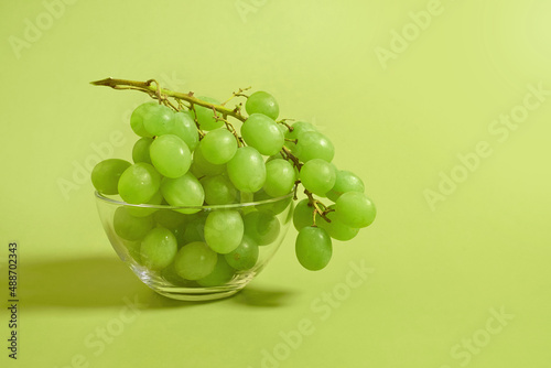 A bunch of green grapes in a glass bowl on a colored background