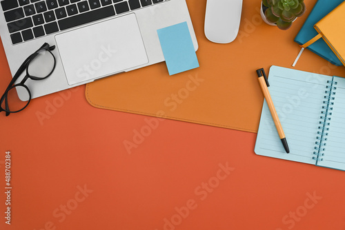 Laptop computer  notebook  sticky note and eyeglasses on orange background.