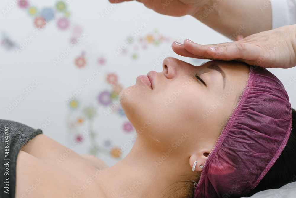Cosmetologist doing anti-aging face massage for young woman in spa salon