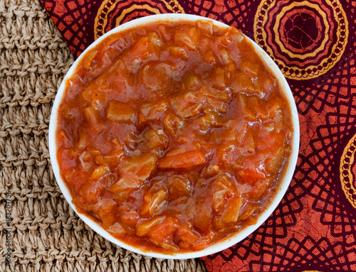 South African vegetable relish or side dish called Chakalaka, originating from townships. flat lay with woven rustic fabric and traditional South African printed cloth