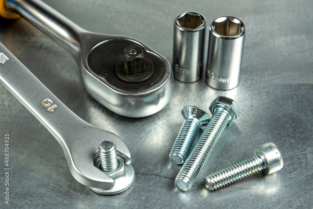 A wrench tightens a metal nut in a steel workpiece. Heads and a ratchet. Close-up. A wrench tightens a metal nut in a steel workpiece. Heads and a ratchet. Close-up.