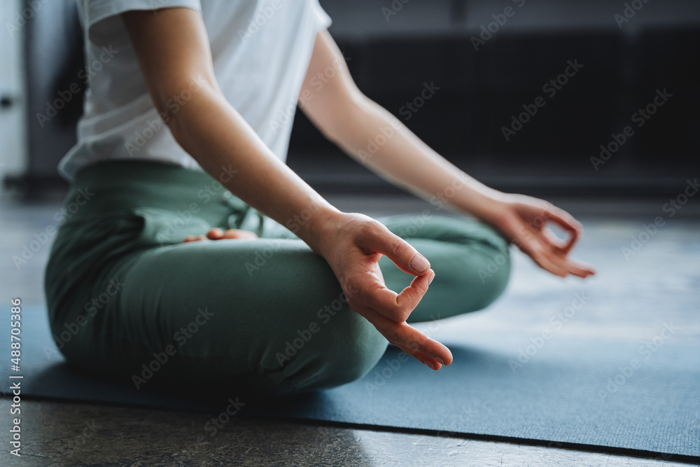 A young girl sits in the lotus position of her hand on her lap, her fingers folded into the rank of mudra. Time of Zen, immersion inward, solitude, alone at home, tranquility and peace.