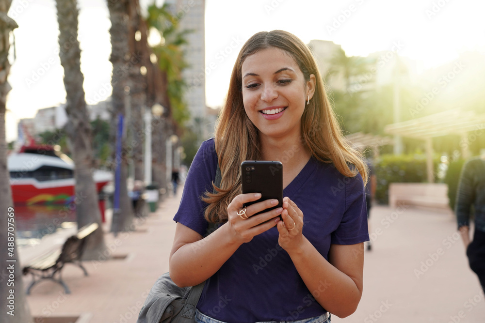 Attractive young woman watching excited her smartphone on city promenade Attractive young woman watching excited her smartphone on city promenade