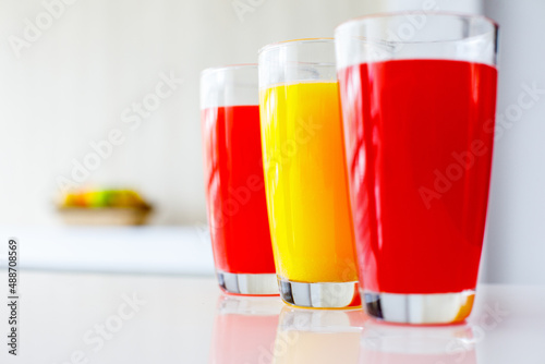 Closeup shot of three tall round glasses of red and yellow cold healthy tasty mixed fresh raw vegetables and fruits juice cocktail soft drink placed on table with copy space and blurred background