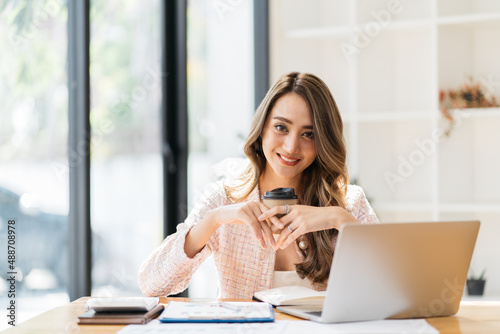 Portrait young attractive beautiful asia female sit on desk smile to camera work at home remotely computer laptop job. College student, employee feel cozy happy in weekend work life balance.