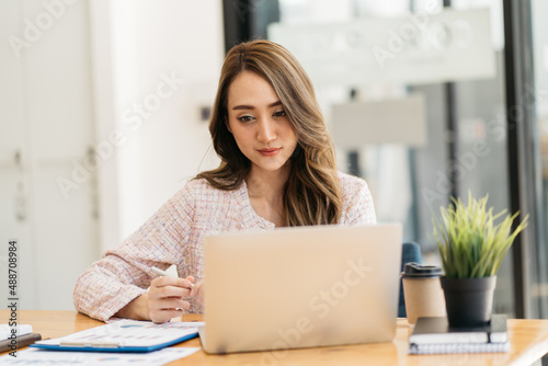 Happy attractive Asian business woman working with a laptop and financial document at office, successful action, Business concept.