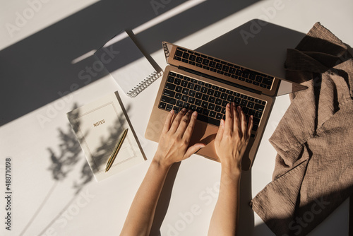 Aesthetic luxury bohemian minimalist home office workspace desk. Woman working on laptop computer. Notebook, blanket, pampas grass with sunlight shadows. Flat lay, top view work, business concept