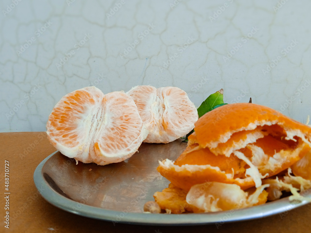 Orange cut into half with it's peel and leaves on a plate with a solid background. Useful for summer, juice or fruit reference.