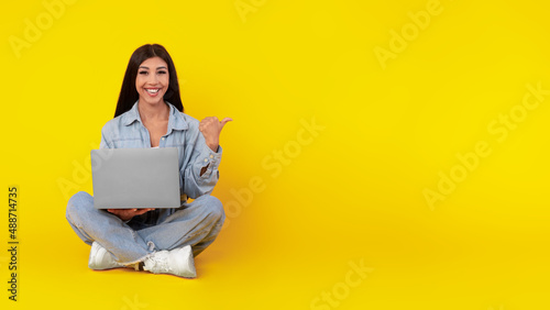 Happy lady using laptop pointing aside at studio photo