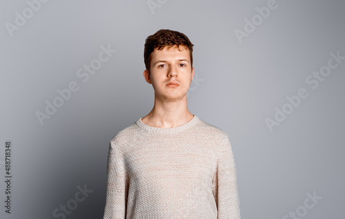 Portrait of a handsome calm teenage boy in sweater over gray background