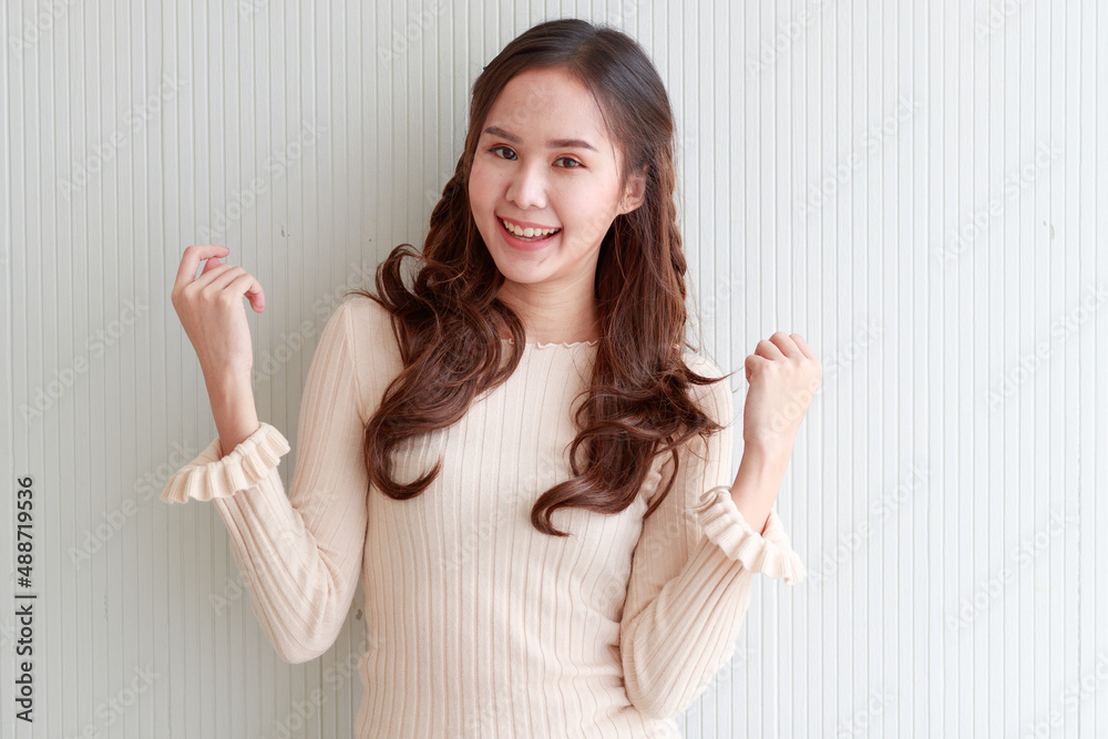 Portrait studio shot Asian young beautiful long brown hair female model in casual long sleeve dress standing posing holding hand up crossed arm smiling look at camera on white stripe wall background Portrait studio shot Asian young beautiful long brown hair female model in casual long sleeve dress standing posing holding hand up crossed arm smiling look at camera on white stripe wall background
