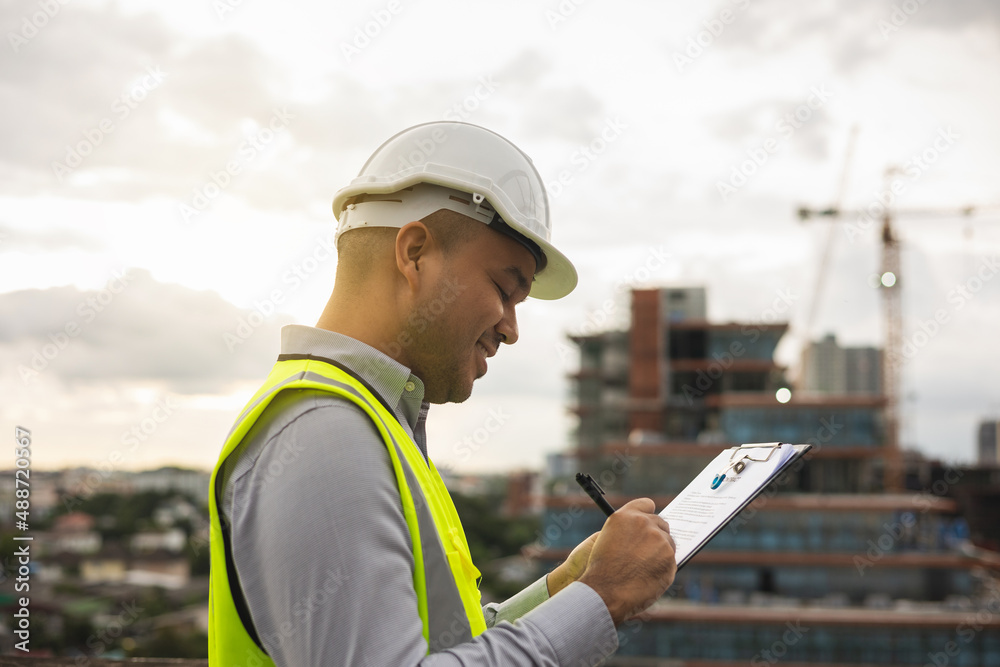 Inspector engineer man or architect with clipboard with white safety helmet in city construction site. Checking with checklist on rooftop building construction at capital. Inspector engineer man or architect with clipboard with white safety helmet in city construction site. Checking with checklist on rooftop building construction at capital.