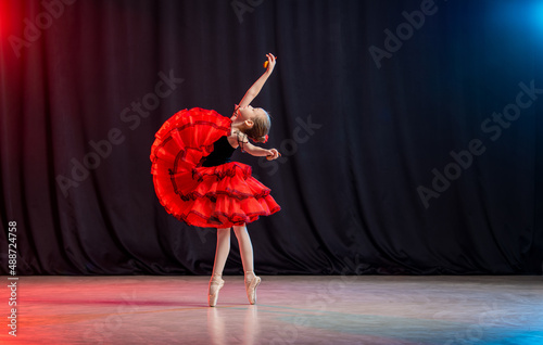 A little girl ballerina is dancing on stage in a tutu on pointe shoes with castanedas, the classic variation of Kitri.