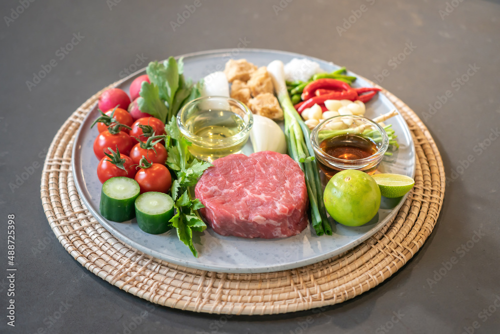 The uncooked ingredients prepared for making yum steak, spicy Thai salad style, are arranged and placed on a local tray set.