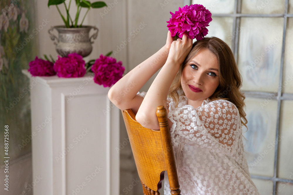 woman in white dress, holding peony bud in her hands, looks at camera. Portrait of beautiful blonde woman. Surprise bouquet of flowers for date, mothers day or valentines day. Place for your text.