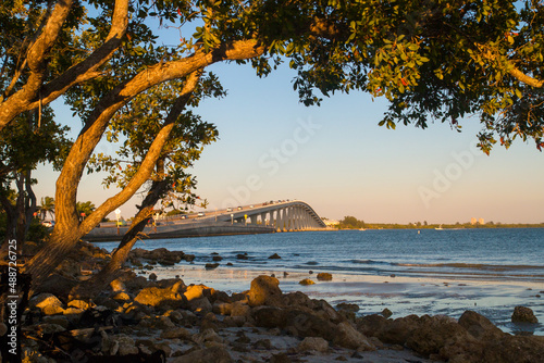 Fort Myers Bridge, Florida, view through the wooden branches tree from the beach on warm afternoon golden sun light, The Sanibel Island Causeway